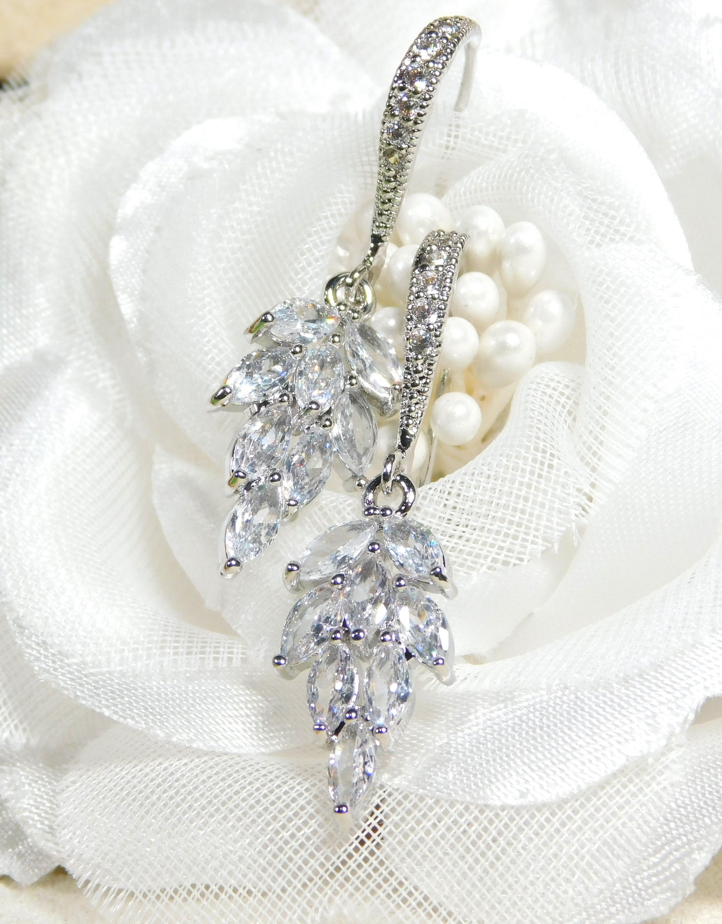Cubic Zirconia leaf dangle earrings on white floral background.